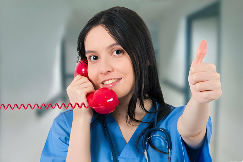 A healthcare worker in scrubs giving a thumbs up while talking on a red telephone.